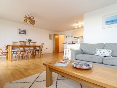 A living room with a wooden dining table and chairs a grey sofa and a wooden coffee table at Ocean Blue in Praa Sands