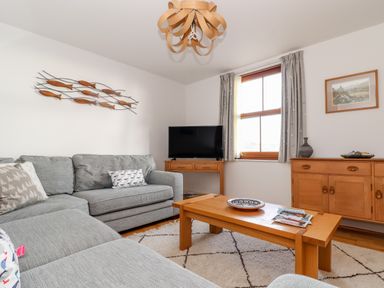 A living room with a gray sofa wooden coffee table wooden sideboard and TV at Ocean Blue in Praa Sands
