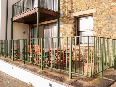 An outdoor patio area with wooden chairs and tables behind a green metal railing at Ocean Blue in Praa Sands