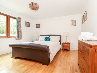 A bedroom with a leather bed white bedding wooden floor and wooden furniture at Ocean Blue in Praa Sands