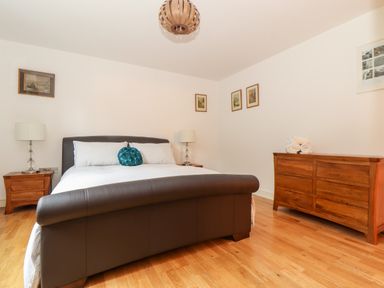 A bedroom with a leather bed a wooden dresser a nightstand with lamps and framed pictures on the walls at Ocean Blue in Praa Sands