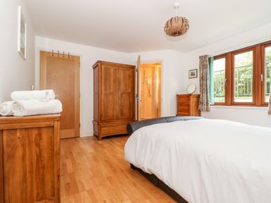 A bedroom with a bed white bedding wooden wardrobe dresser and window with curtains at Ocean Blue in Praa Sands