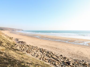 A wide sandy beach with rocks in the foreground and the ocean in the background at Ocean Blue in Praa Sands