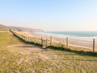 A coastal path with grass and a fenced wooden gate overlooking a sandy beach and ocean at Ocean Blue in Praa Sands