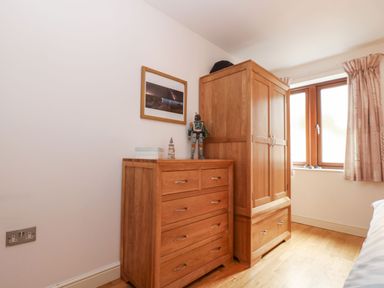 A bedroom corner with a wooden chest of drawers, a wooden wardrobe, a window with curtains, and a framed picture on the wall at Ocean Blue in Praa Sands