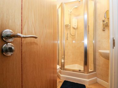 A bathroom with a shower cubicle a sink a mirror and a door slightly open at Ocean Blue in Praa Sands