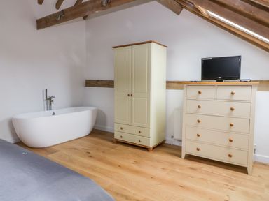 A room with a bathtub wardrobe dresser with a television on top and wooden exposed ceiling beams at Grange Barn Gedding near Felsham