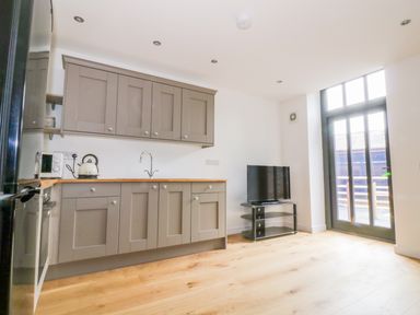 A kitchen with brown cabinets a kettle microwave a television on a stand and tall windows at Grange Barn in Gedding near Felsham