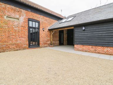 An outdoor courtyard with gravel ground and brick and black wooden buildings at Grange Barn in Gedding near Felsham