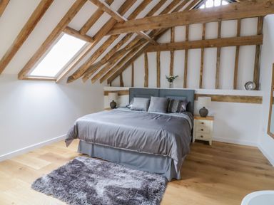 A bedroom with a bed and bedside tables under exposed wooden beams at Grange Barn in Gedding near Felsham