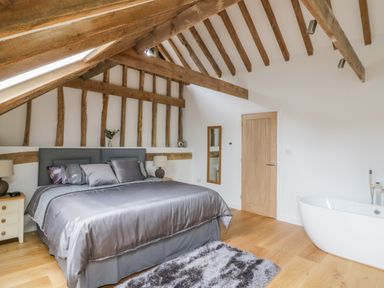 A bedroom with a bed bedside tables lamps a mirror wooden beams and a bathtub at Grange Barn in Gedding near Felsham