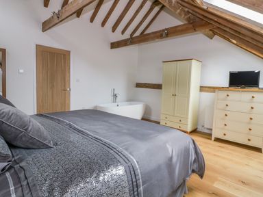 A bedroom with a double bed a bath a wardrobe a chest of drawers and exposed wooden beams at Grange Barn in Gedding near Felsham