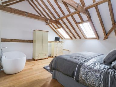 A bedroom with a bed a wardrobe a chest of drawers a bathtub and exposed wooden beams in the ceiling at Grange Barn in Gedding near Felsham