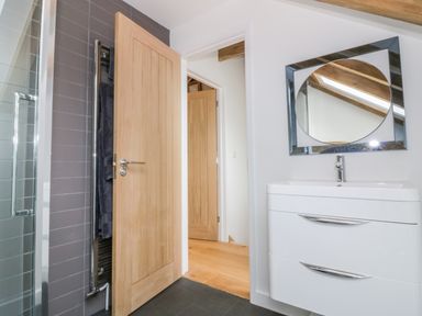 A bathroom with a wooden door open to a hallway and a white sink with a mirror above it at Grange Barn in Gedding near Felsham