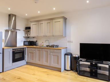 A kitchen with grey cabinets microwave kettle oven and a television on a stand at Grange Barn in Gedding near Felsham