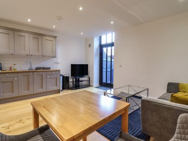 A kitchen and living area with wooden table chairs sofa glass coffee table and television at Grange Barn in Gedding near Felsham