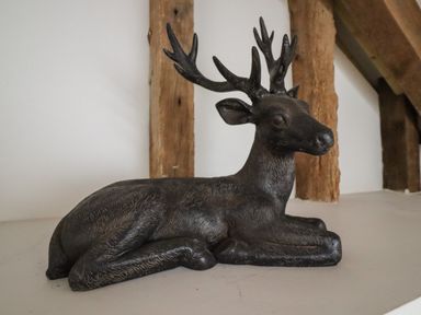 A black statue of a deer with antlers lying down on a white surface with wooden beams in the background at Grange Barn in Gedding near Felsham