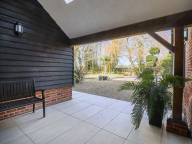 A covered patio area with a black bench and potted plant overlooking a gravel garden at Grange Barn in Gedding near Felsham