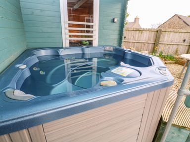 An outdoor hot tub next to a turquoise wooden wall with a window at Borah Lodge in Mousehole