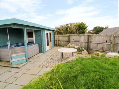 A backyard with a hot tub under a covered structure and a round table on gravel at Borah Lodge in Mousehole