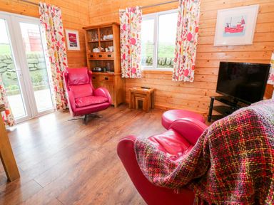 A living room with red leather chairs a wooden cabinet colorful curtains and a TV at Borah Lodge Mousehole
