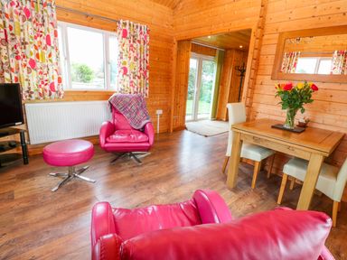 A living room with wooden walls red chairs a table with flowers and floral curtains at Borah Lodge in Mousehole