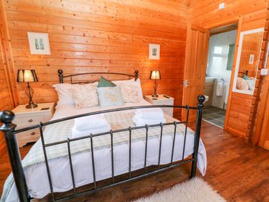 A bedroom with a black metal bed frame two nightstands with lamps and an open door leading to a bathroom at Borah Lodge in Mousehole