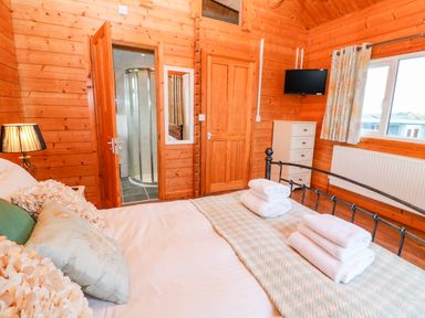 A bedroom with a made bed with folded towels a bedside lamp a wall-mounted television a window and wooden walls at Borah Lodge in Mousehole