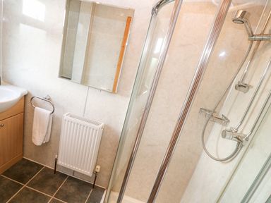 A bathroom with a shower enclosure sink with cabinet towel rail radiator and mirror at Borah Lodge in Mousehole