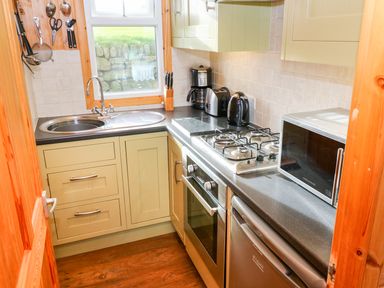 A small kitchen with a sink a gas stove an oven a microwave a coffee maker a toaster and kitchen utensils at Borah Lodge in Mousehole