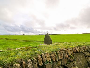 A rural green field with a stone wall and a standing stone in the center at Borah Lodge in Mousehole