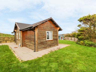 A wooden cabin with a tiled patio and grassy yard at Borah Lodge in Mousehole