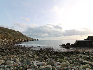 A rocky shoreline with a hill on the left and a stone structure on the right by the sea at Borah Lodge in Mousehole
