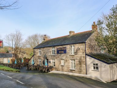 An outdoor seating area with tables and umbrellas in front of a stone building named Lamorna Wink