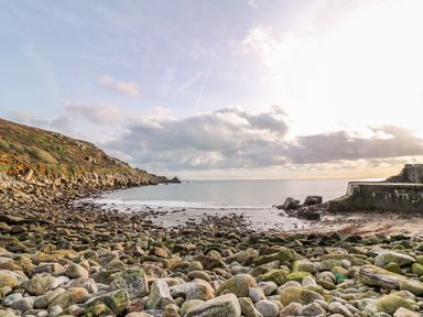 A rocky beach with a stone pier and a hillside at Meadowside in Mousehole