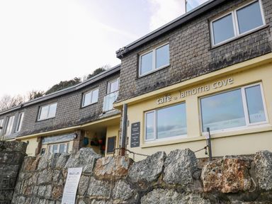 Exterior view of a building with a stone wall in front and cafe lamorna cove signage on the building