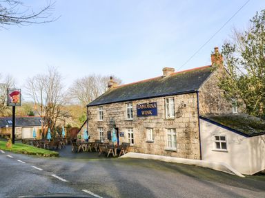 A stone building with outdoor seating and blue umbrellas by a road at Lamorna Wink