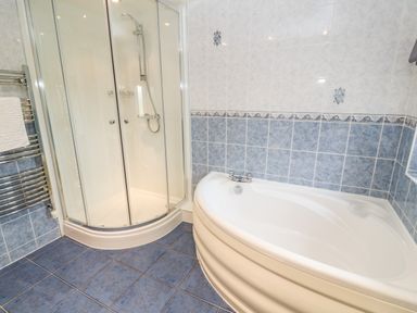 A bathroom with a white corner bathtub and a glass-enclosed shower at Meadowside in Mousehole