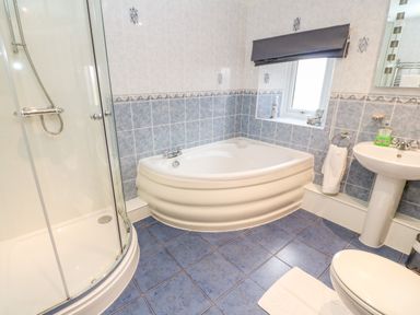 A bathroom with a corner bathtub shower enclosure sink toilet and blue tiled floor at Meadowside in Mousehole