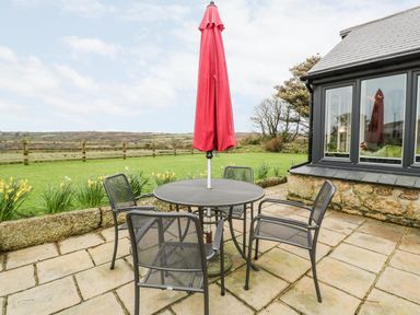 An outdoor patio with a round metal table and four chairs with a closed red umbrella at Meadowside in Mousehole