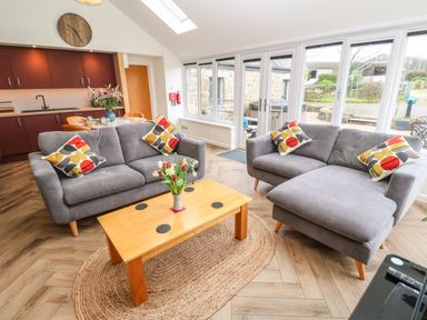 A living room with two gray sofas and pillows a wooden coffee table with flowers and large windows at Meadowside in Mousehole