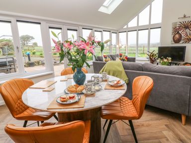 A dining area with a round table and leather chairs next to a living room with gray sofas and a television at Meadowside in Mousehole