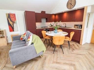 A kitchen and living area with maroon cabinets a round dining table with chairs and a gray sofa at Meadowside in Mousehole