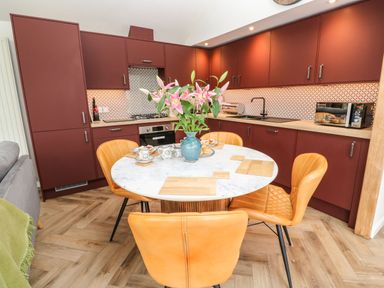 A kitchen with red cabinets a round marble table with flowers and orange chairs at Meadowside in Mousehole