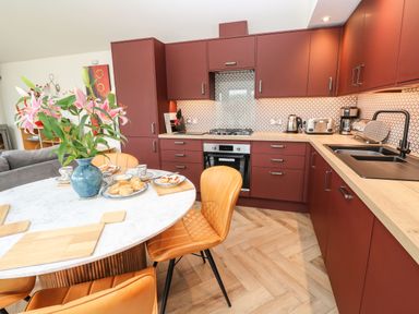 A kitchen with maroon cabinets and wooden countertops a round white table with flowers and food on it at Meadowside in Mousehole