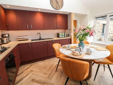 A kitchen with maroon cabinets a round dining table with flowers and tea set at Meadowside in Mousehole