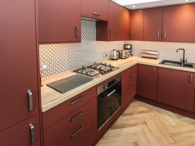 A kitchen with red cabinets wooden countertop a gas stove oven sink and small appliances at Meadowside in Mousehole