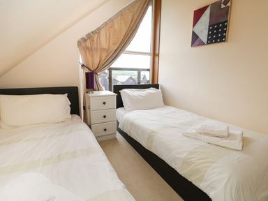 A bedroom with two single beds a small white nightstand and a window with curtains at Willow Retallack in Retallack near St Columb Major
