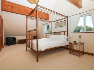 A bedroom with a four-poster bed side table a black armchair wooden chest windows with curtains and wooden beams at Willow Retallack in Retallack near St Columb Major