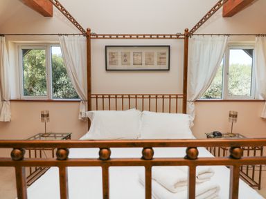 A bedroom with a metal four-poster bed two windows and bedside tables with lamps at Willow Retallack in Retallack near St Columb Major